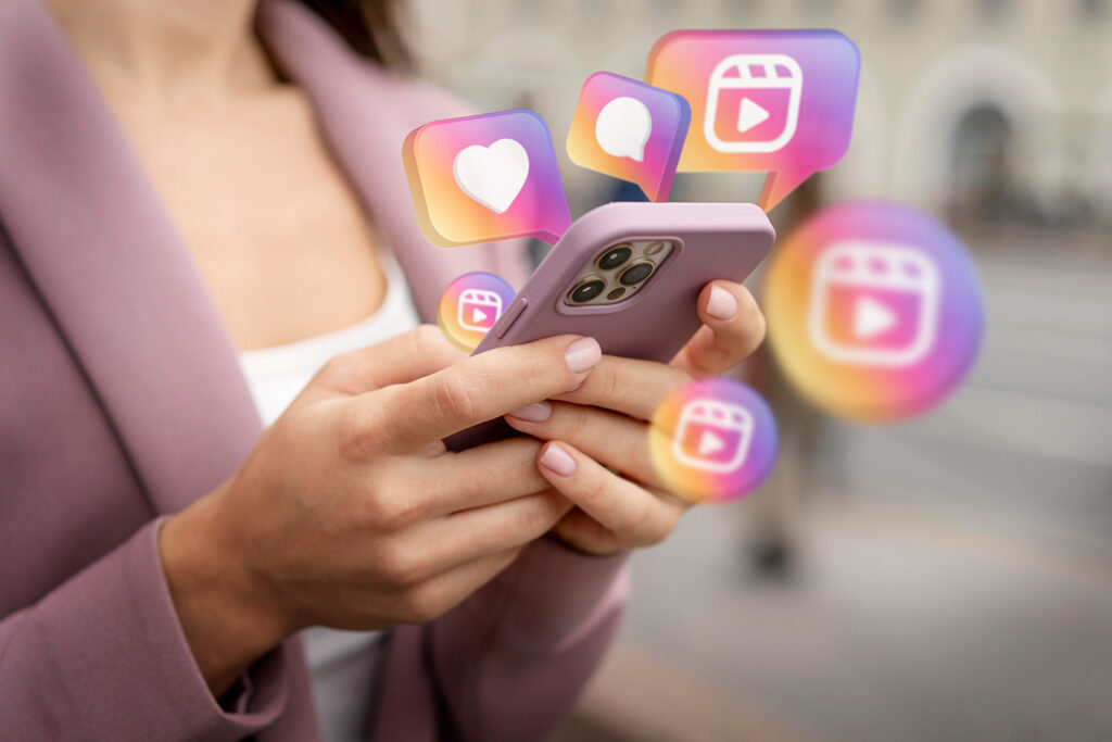 Mãos segurando celular com ícones de curtidas, comentários e notificações das redes sociais, representando o Módulo Mídia do Template Track